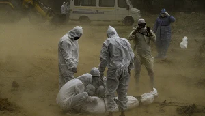 Osoby w kombinezonach ochronnych nad ciałem zmarłego na COVID-19, Indie, New Dehli, maj 2020