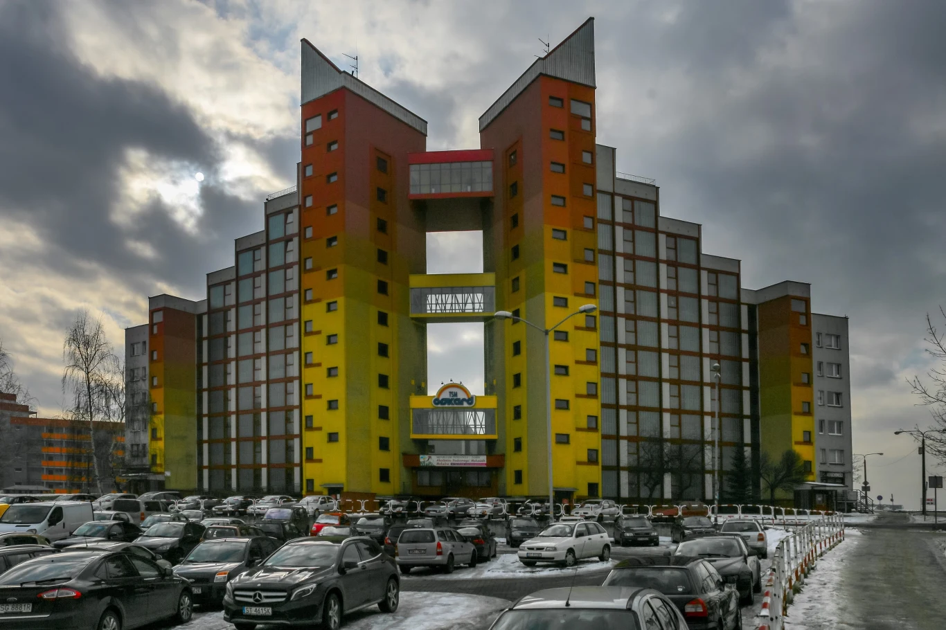 Brama Słońca w Tychach - ta nietypowa budowla stanowi wizytówkę śląskiego miasta. Może się podobać lub wzbudzać śmiech, z pewnością jednak wyróżnia się spośród otaczającej ją szarej socrealistycznej zabudowy. Brama Słońca leży przy ulicy Dmowskiego w Tychach. Składa się z dwóch uskokowych bloków zakończonych wieżami i połączonych przejściowymi klatkami schodowymi. Gradient zaczynający się od bladożółtego, a zakończony kolorem bordowym kojarzy się z zachodzącym słońcem. Brama Słońca w Tychach - ta nietypowa budowla stanowi wizytówkę śląskiego miasta. Może się podobać lub wzbudzać śmiech, z pewnością jednak wyróżnia się spośród otaczającej ją szarej socrealistycznej zabudowy. Brama Słońca leży przy ulicy Dmowskiego w Tychach. Składa się z dwóch uskokowych bloków zakończonych wieżami i połączonych przejściowymi klatkami schodowymi. Gradient zaczynający się od bladożółtego, a zakończony kolorem bordowym kojarzy się z zachodzącym słońcem.