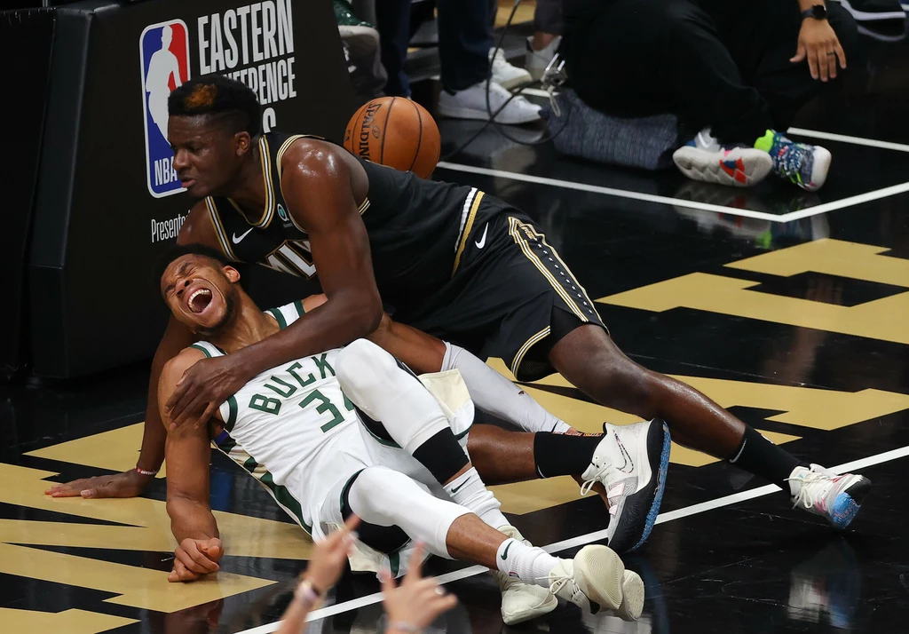 Giannis Antetokounmpo (w białym stroju) po próbie zablokowania centra Hawks, Clinta Capeli, padł na parkiet z grymasem bólu na twarzy
