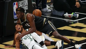 Giannis Antetokounmpo (w białym stroju) po próbie zablokowania centra Hawks, Clinta Capeli, padł na parkiet z grymasem bólu na twarzy