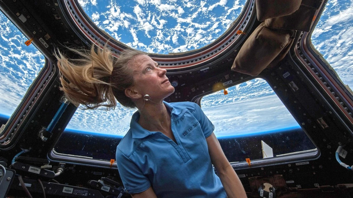 Gdy na ISS mija dokładnie 60 sekund, na powierzchni Ziemi upływa około 60,000000017 sekundy Astronautka w stanie nieważkości w przeszklonym module ISS z widokiem na Ziemię i chmury za iluminatorami.