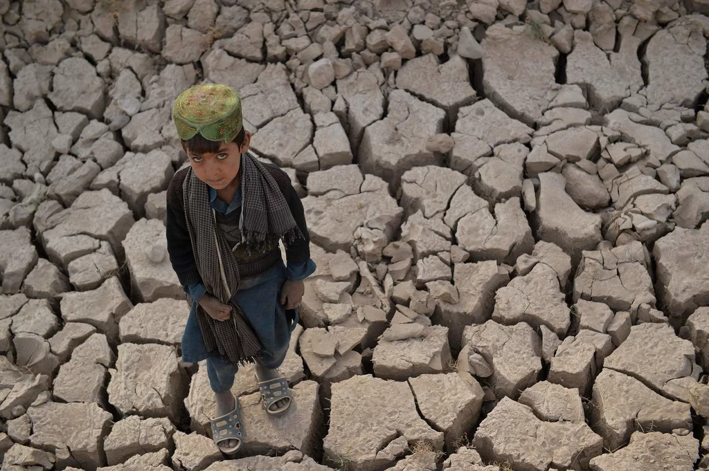 Dziecko stojące na wyschniętej ziemi w nękanym suszą wynikającą ze zmian klimatu Afganistanie.