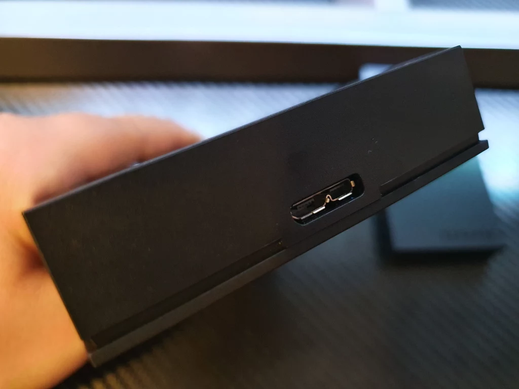 Na froncie wzrok przykuwają dwa tłoczone logotypy marek Xbox oraz Seagate, które umiejscowiono po przeciwległych stronach. Na jednej z bocznych krawędzi zlokalizowano port USB Micro typu B oraz podświetlaną na biało niewielką diodę, która daje znać o działaniu dysku. Irlandzka korporacja postarała się, by sprzęt nie tylko służył jak należy, ale także wyglądał stylowo i przede wszystkim nawiązywał do konsoli Giganta z Redmond. Efekt jest więcej niż zadowalający - Seagate HDD Game Drive for Xbox pod względem designu doskonale współgra z konsolą Xbox Series X. Trudno nie zauważyć niemal identycznego wzornictwa, podobnych materiałów, jakby oba sprzęty zeszły z tej samej linii produkcyjnej. A dla wzmocnienia wrażeń, tak by nikt nie miał wątpliwości, co do współpracy z jakim urządzeniem zaprojektowany został dysk, po drugiej stronie, na całej długości krawędzi umieszczono pasek LED o charakterystycznym zielonym kolorze, który podświetla się w momencie uruchomienia dysku. Na froncie wzrok przykuwają dwa tłoczone logotypy marek Xbox oraz Seagate, które umiejscowiono po przeciwległych stronach. Na jednej z bocznych krawędzi zlokalizowano port USB Micro typu B oraz podświetlaną na biało niewielką diodę, która daje znać o działaniu dysku. Irlandzka korporacja postarała się, by sprzęt nie tylko służył jak należy, ale także wyglądał stylowo i przede wszystkim nawiązywał do konsoli Giganta z Redmond. Efekt jest więcej niż zadowalający - Seagate HDD Game Drive for Xbox pod względem designu doskonale współgra z konsolą Xbox Series X. Trudno nie zauważyć niemal identycznego wzornictwa, podobnych materiałów, jakby oba sprzęty zeszły z tej samej linii produkcyjnej. A dla wzmocnienia wrażeń, tak by nikt nie miał wątpliwości, co do współpracy z jakim urządzeniem zaprojektowany został dysk, po drugiej stronie, na całej długości krawędzi umieszczono pasek LED o charakterystycznym zielonym kolorze, który podświetla się w momencie uruchomienia dysku.