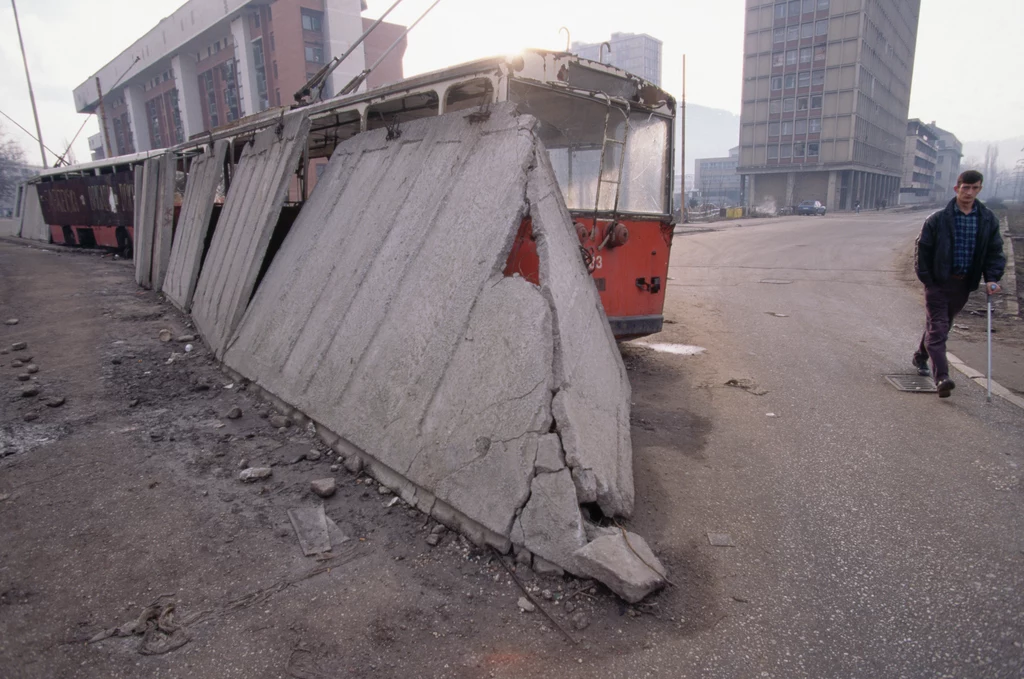 Uszkodzona barykada z betonu i starych wagonów tramwajowych zagradzająca część Alei Snajperów Sarajewie 