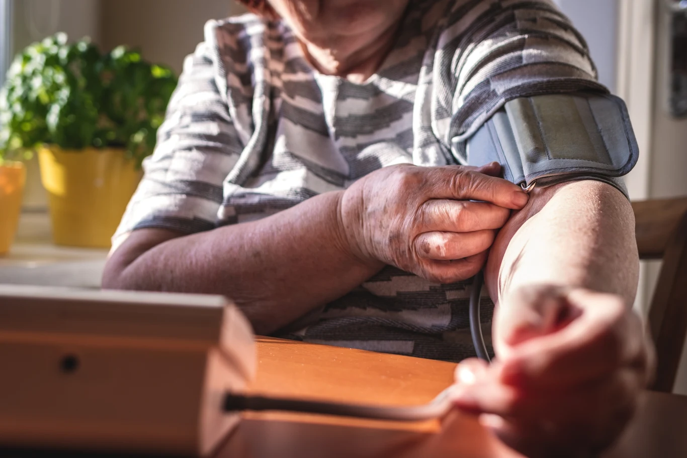 Zdarza się jednak, że niskie ciśnienie jest objawem poważniejszych problemów, np. chorób serca czy zaburzeń hormonalnych Starsza osoba w paskowanej bluzce zakłada mankiet ciśnieniomierza na przedramię przy stole w nasłonecznionym pomieszczeniu.