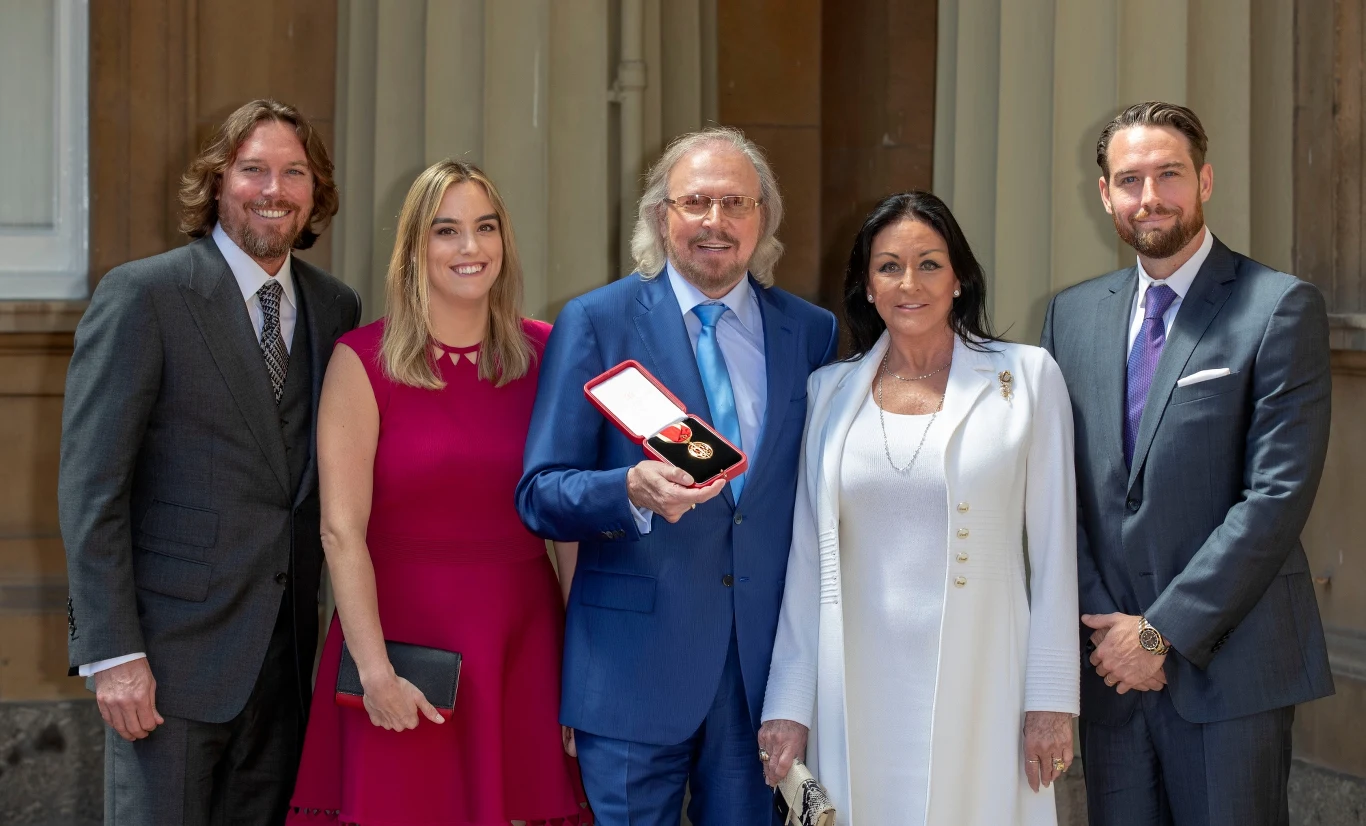 Barry Gibb otrzymał tytuł szlachecki w 2018 r. Na zdjęciu wokalista Bee Gees razem ze swoją żoną Lindą i dziećmi: Michaelem (z prawej), Alexandrą i Ashleyem (z lewej). Barry Gibb otrzymał tytuł szlachecki w 2018 r. Na zdjęciu wokalista Bee Gees razem ze swoją żoną Lindą i dziećmi: Michaelem (z prawej), Alexandrą i Ashleyem (z lewej).