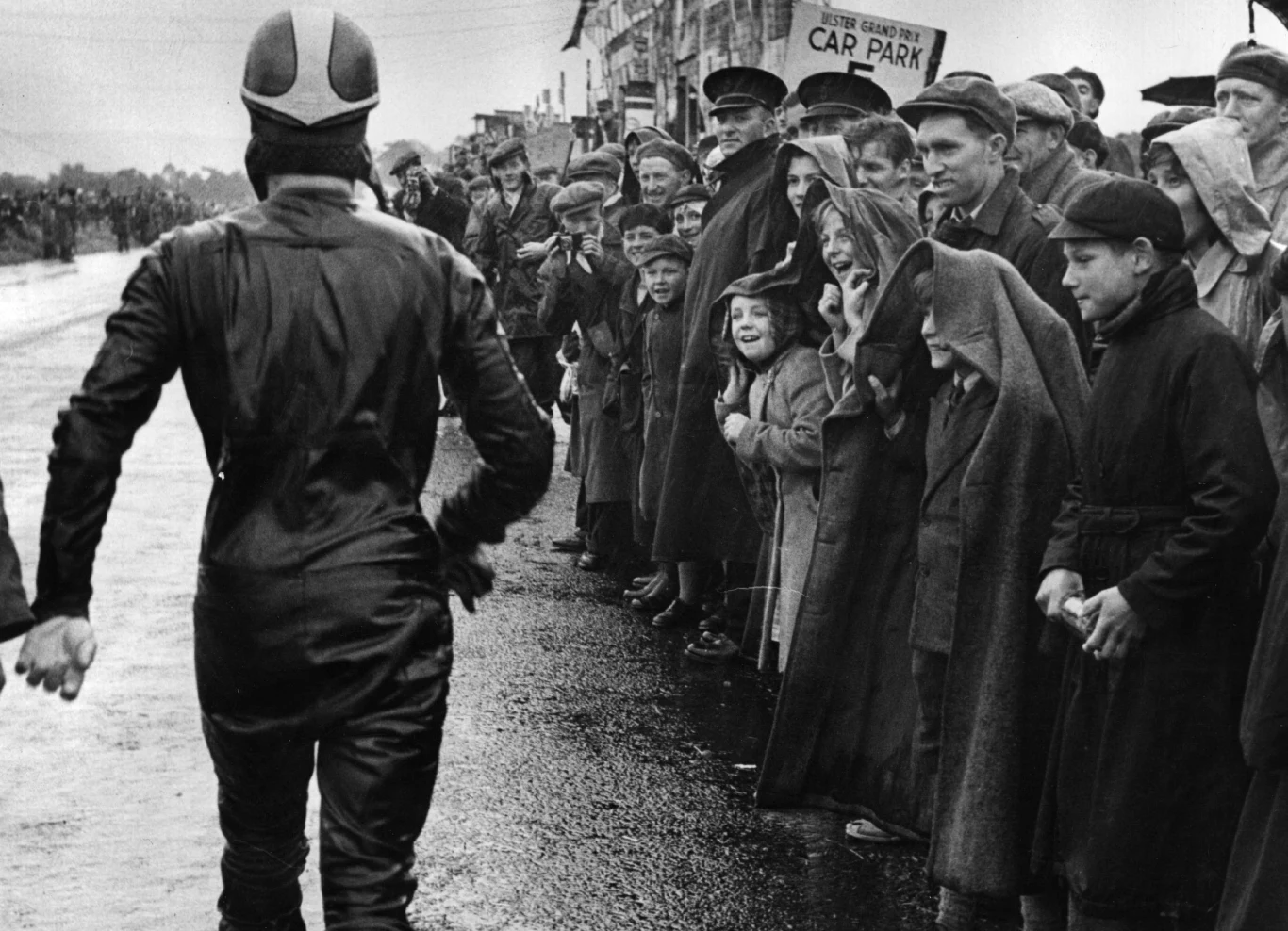 Tłumy wiwatują na cześć żużlowca, który idzie w kierunku oficjalnej trybuny. Tłumy wiwatują na cześć żużlowca, który idzie w kierunku oficjalnej trybuny.