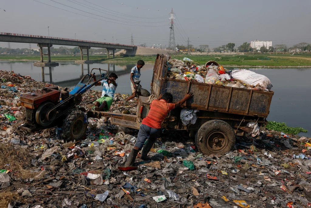 Pracownicy wyrzucają odpady na wysypisko znajdujące się tuż obok rzeki Dhaleshwari, z której woda wpływa do rzeki Buriganga, 20 kwietnia 2023 roku