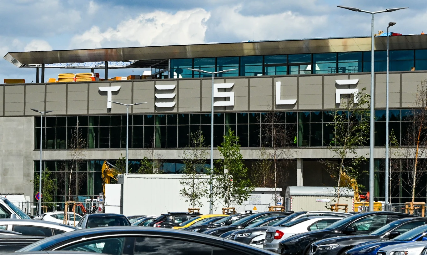 W pod berlińskiej fabryce Tesli szykują się tysiące nowych miejsc pracy Fabryka Tesli pod Berlinem z dużym logo, parking z samochodami, widoczne maszyny budowlane i infrastruktura.