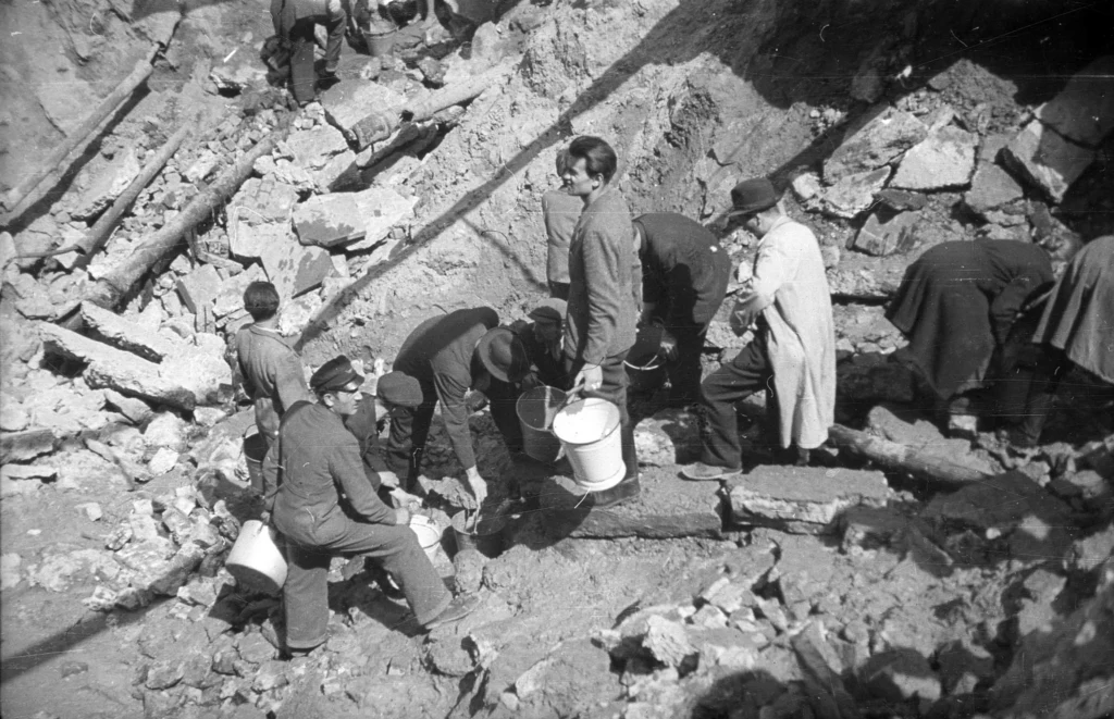 Ludność cywilna czerpiąca wodę z rur w leju po bombie na skrzyżowaniu ulic Zielnej i Złotej, 14 sierpnia 1944 r.