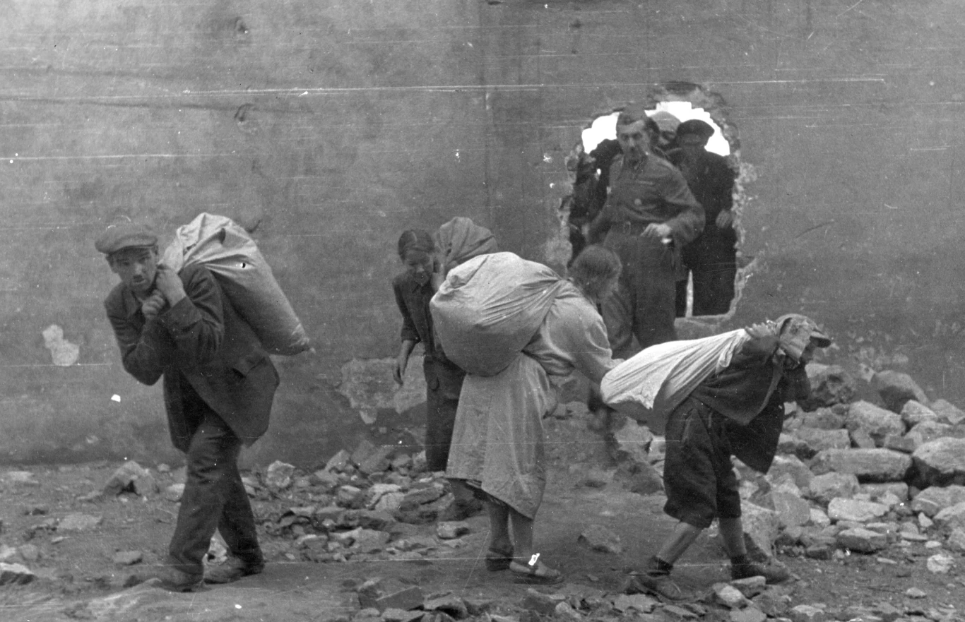 Ludność cywilna wynosząca worki z pszenicą przez wybitą dziurę w murze, sierpień 1944 r. 