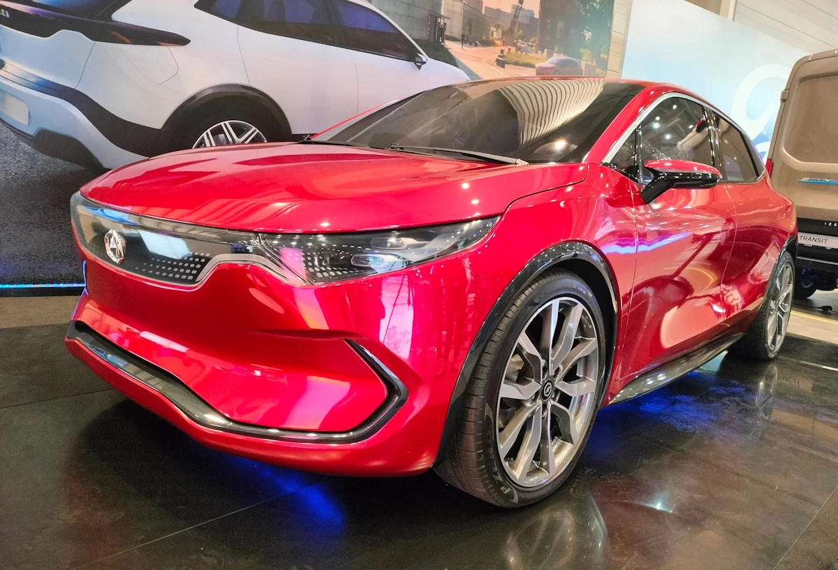 Wybrano strategicznego partnera technologicznego dla spółki ElectroMobility Poland w kontekście budowy hubu elektromobilności w Jaworznie (zdj. ilustracyjne) Czerwony sportowy samochód elektryczny coupe na wystawie, na tle grafiki z nowoczesnymi autami.