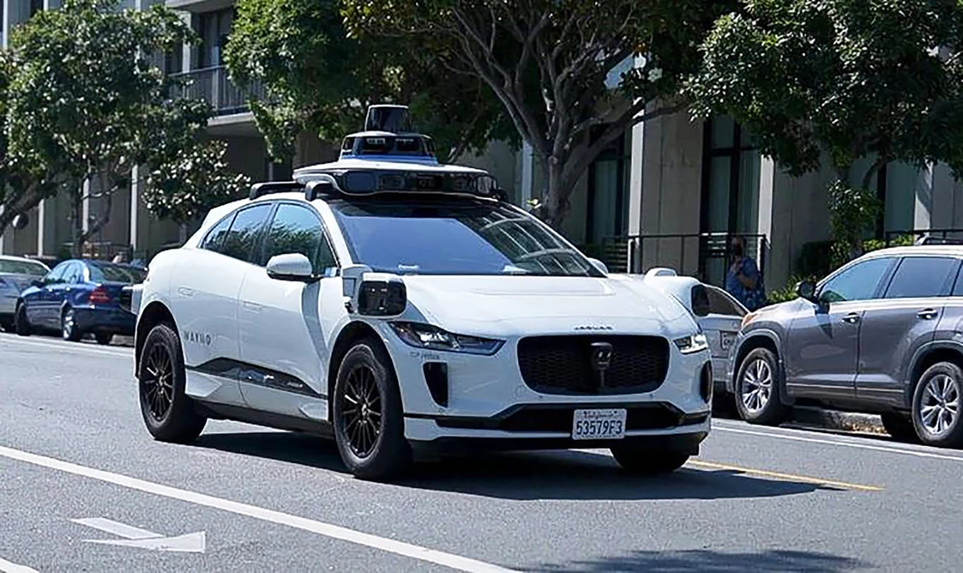 Do tej pory policja nie miała narzędzi, aby wystawiać mandaty za łamanie przepisów przez pojazd autonomiczny Autonomiczna taksówka Jaguar I-Pace z czujnikami na dachu na miejskiej ulicy, w tle auta i budynki.