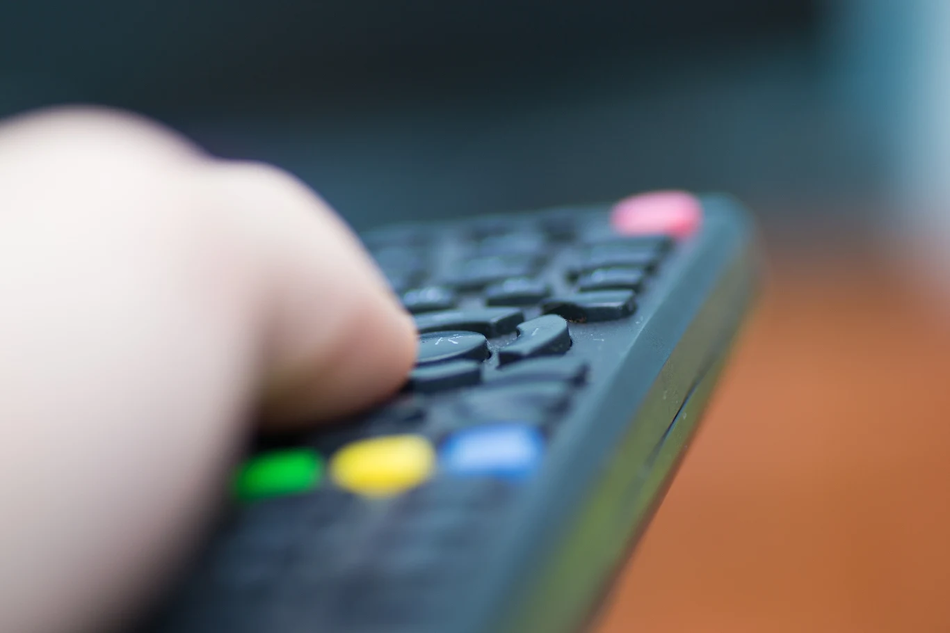 Pilot zdalnego sterowania telewizorem w ręce. Na zdjęciu widać dłoń trzymającą pilot do telewizora, który zwrócony jest w stronę odbiornika. Resztę zdjęcia pokrywa blur.