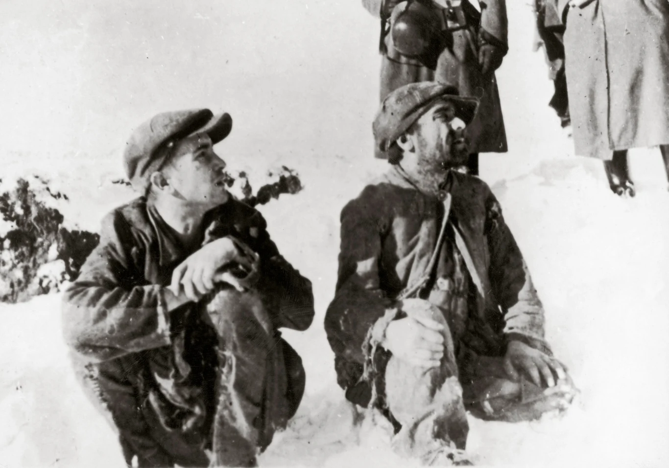 Zdjęcie opisane jako: Polscy Żydzi siedzący w śniegu, w tle niemieccy żołnierze, Bełżec 1942 r. (uwagę zwraca, że mężczyźni nie mają opasek z gwiazdą Dawida)