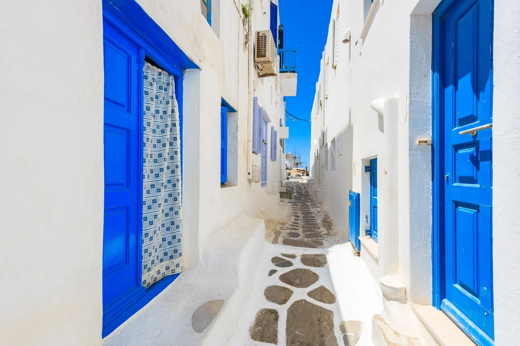 Charakterystycznym krajobrazem miasteczek greckiej wyspy Mykonos są wąskie uliczki i białe budynki z niebieskimi akcentami 