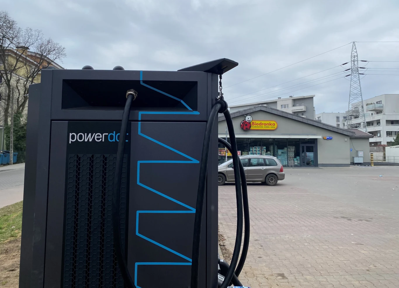 Ładowarka firmy Powerdot ustawiona na parkingu sklepu z widokiem na Biedronkę.