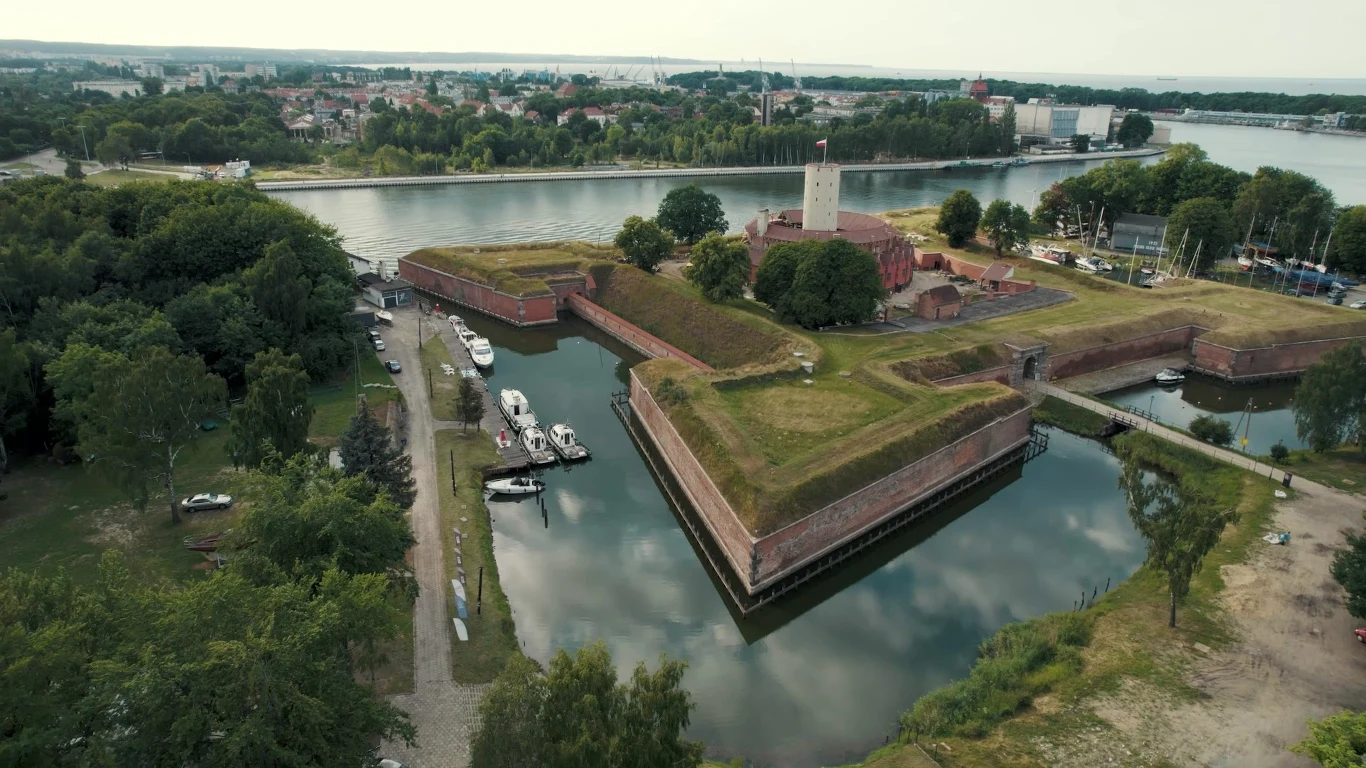 Twierdza Wisłoujście widok z drona. W centrum biała wieża, na zewnątrz ceglane kamieniczki, dziedziniec oraz 4 bastiony. Twierdza Wisłoujście widok z drona. W centrum biała wieża, na zewnątrz ceglane kamieniczki, dziedziniec oraz 4 bastiony.