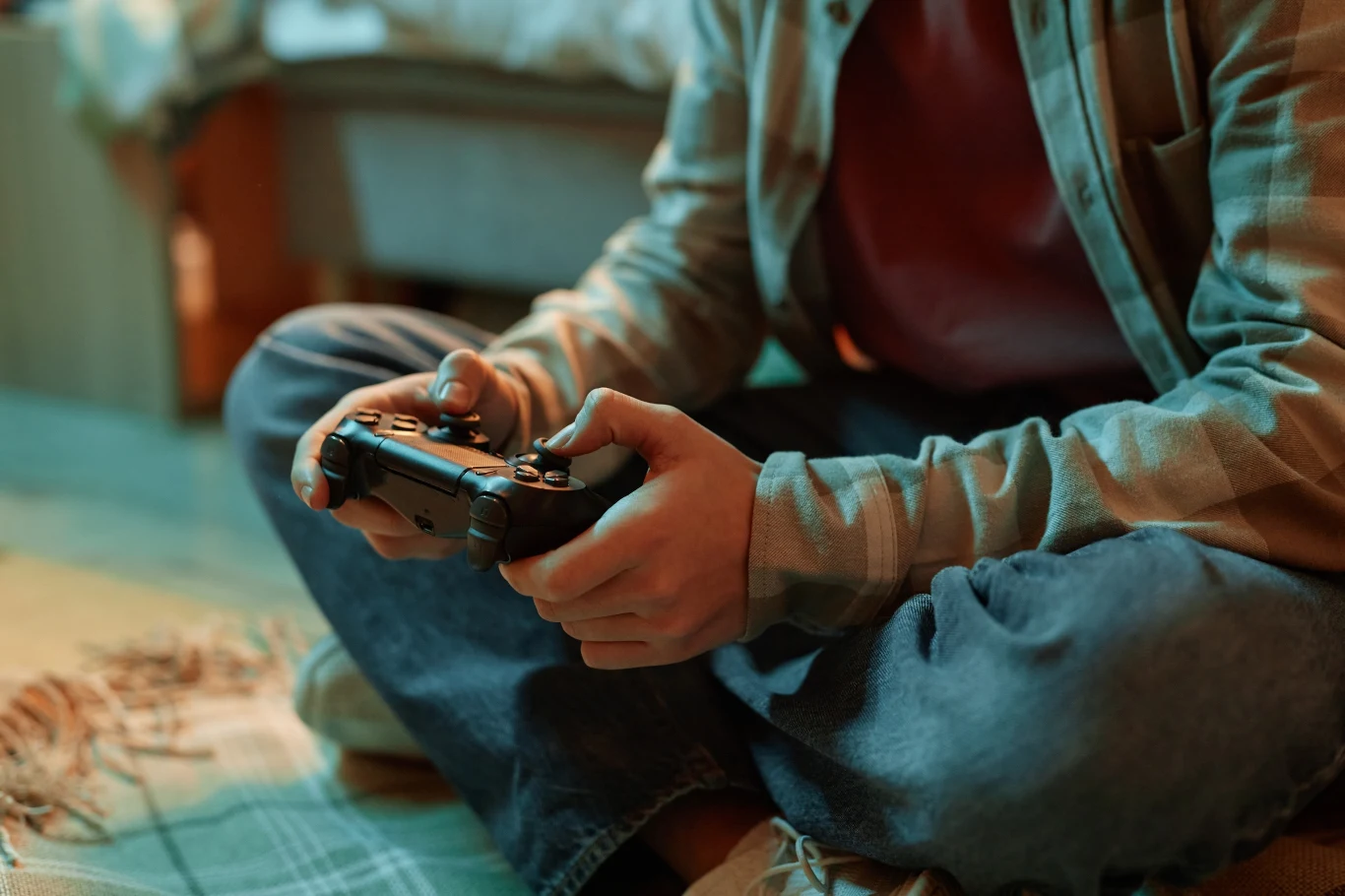 Sony kombinuje z cenami gier w Polsce. Po zalogowaniu promocja nagle się zmienia Osoba siedzi po turecku na podłodze, trzyma czarny kontroler do gier w domowym wnętrzu, koc w tle.