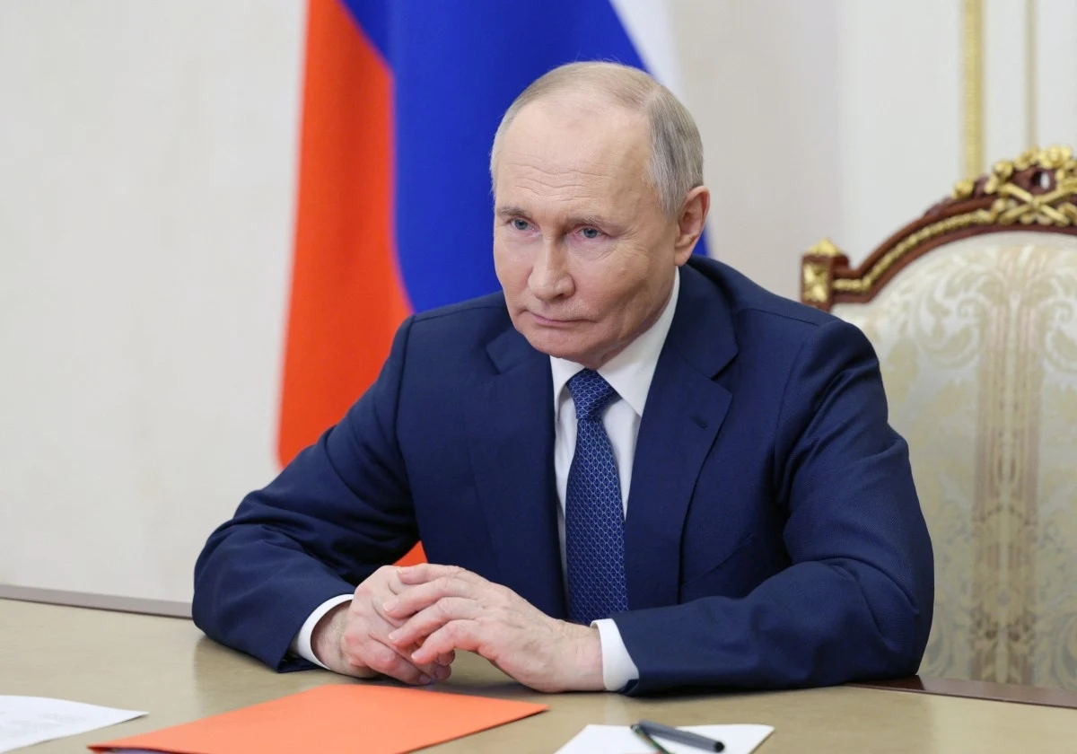Media: Putin podpisał trzy tajne dekrety Władimir Putin w garniturze przy stole z pomarańczową teczką i długopisem, w tle flaga.