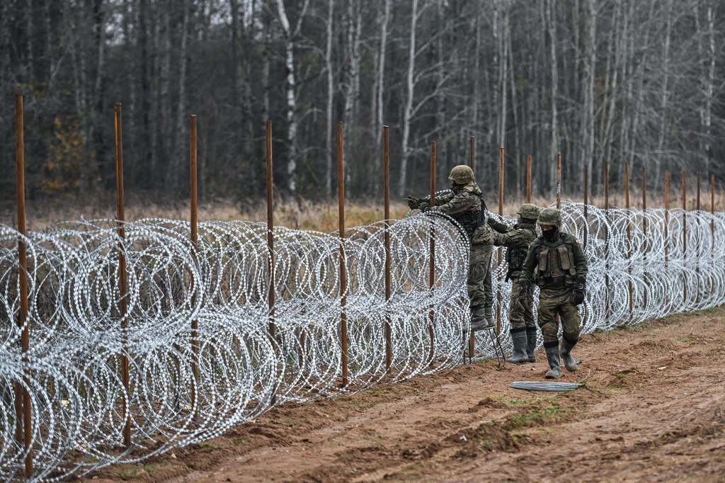 Polscy żołnierze rozkładający mur z drutu kolczastego na granicy polsko-białoruskiej 