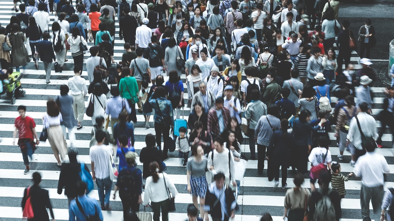 Tłum ludzi na przejściu dla pieszych w mieście, widoczny różnorodny ubiór przechodniów.