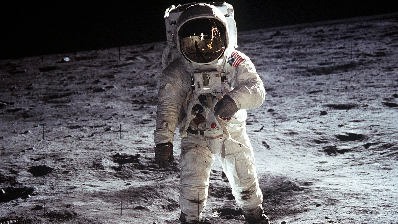 Astronaut Buzz Aldrin specerujący po powierzchni Księżyca Astronauta Buzz Aldrin w skafandrze kosmicznym stoi na powierzchni Księżyca. W hełmie widać odbicie fotografa.