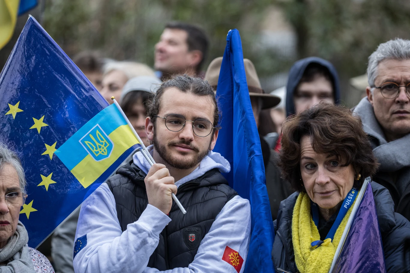 UE może wprowadzić zmiany dla ukraińskich mężczyzn Grupa osób na zgromadzeniu z flagami Unii Europejskiej i Ukrainy, młody mężczyzna i starsza kobieta na pierwszym planie.