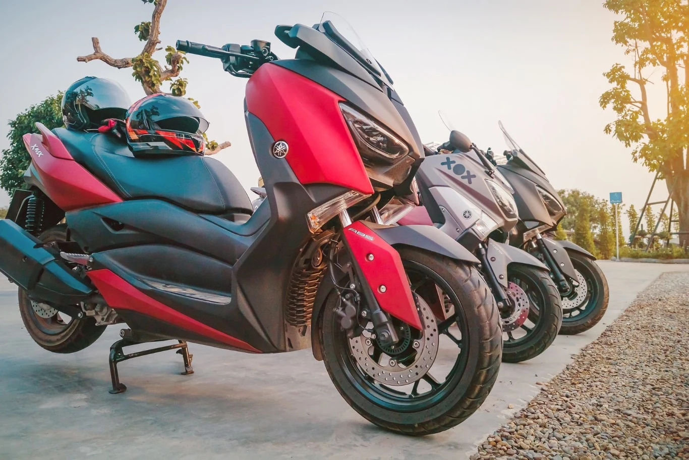 Czy na skuter 50 i 125 cm3 trzeba mieć kask i prawo jazdy? Motocykle 50 i 125 cm3 zaparkowane na placu, czerwony z kaskiem na siedzeniu, o zmierzchu.