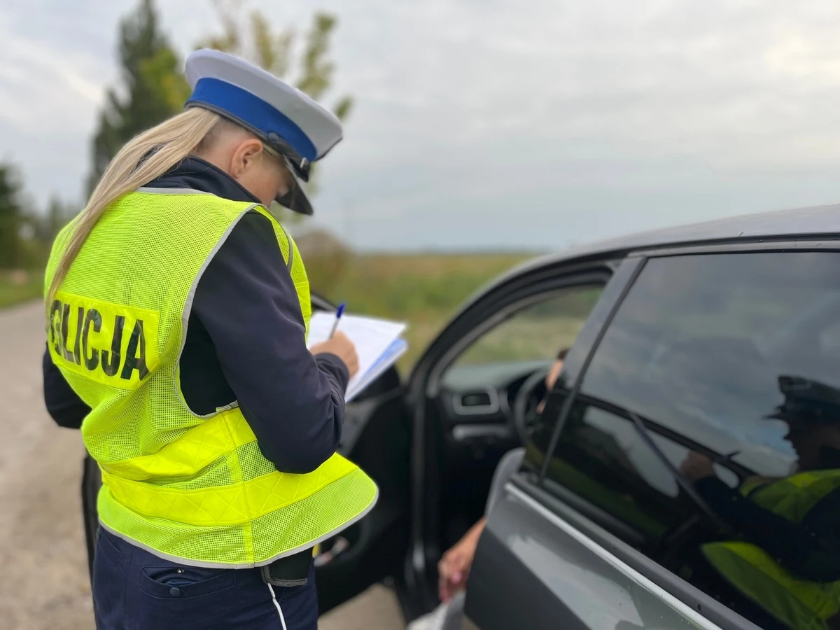 Nowe przepisy wprowadzają surowy okres próbny dla początkujących kierowców Policjantka w odblaskowej kamizelce sporządza notatki w dokumentach podczas kontroli drogowej.