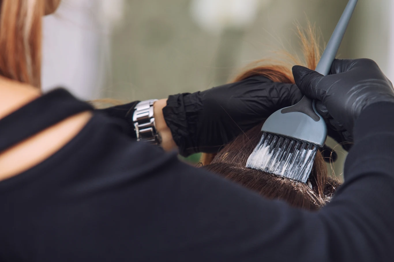 Według fryzjerów na jesień nie będą modne płaskie brązy i zbyt jasne blondy Fryzjerka w rękawiczkach nakłada farbę pędzlem na włosy klientki, widoczny zegarek na nadgarstku.