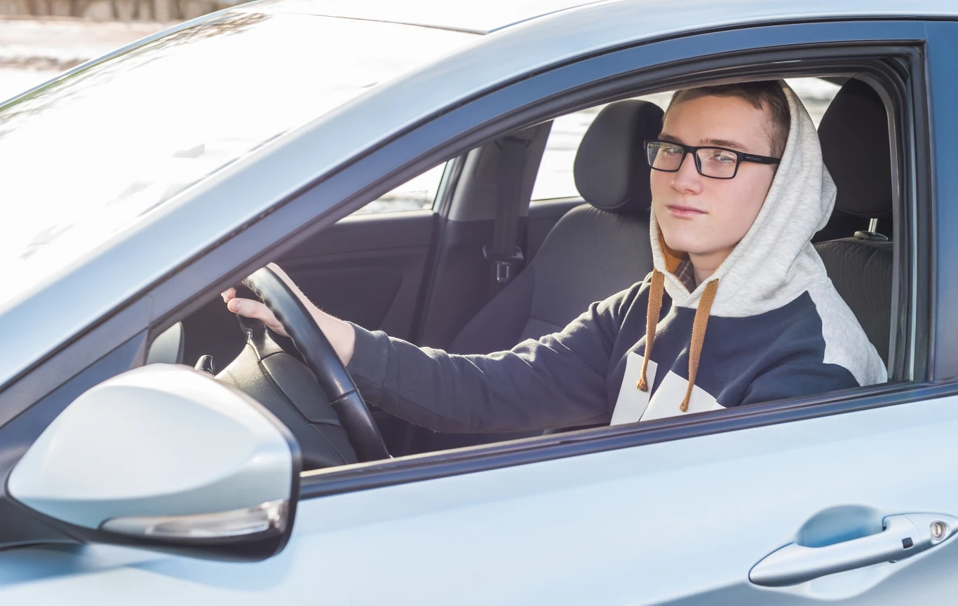 Młody mężczyzna prowadzi samochód w okularach.