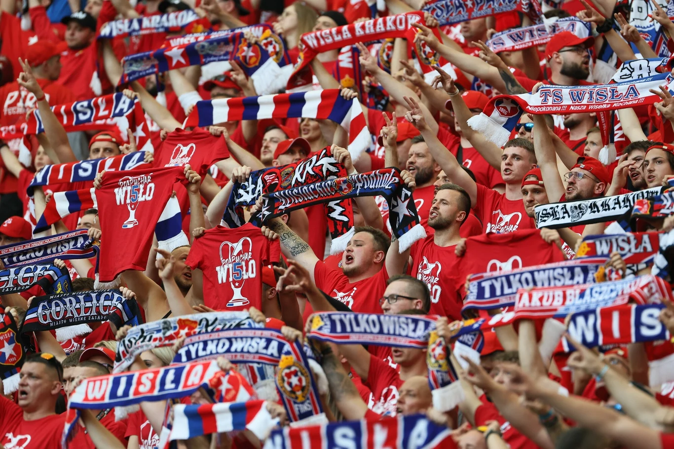 Kibice Wisły Kraków Kibice Wisły Kraków w czerwonych koszulkach i szalikach z napisem Wisła Kraków na stadionie piłkarskim.