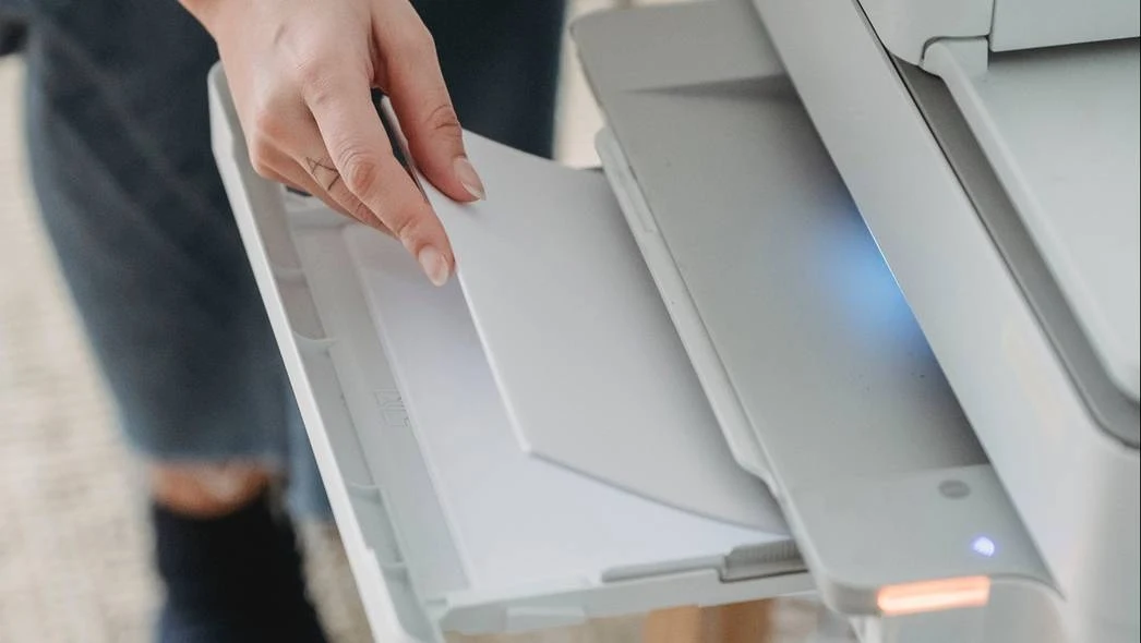 Ręka wkładająca papier do drukarki biurowej, gotowa do drukowania dokumentów.