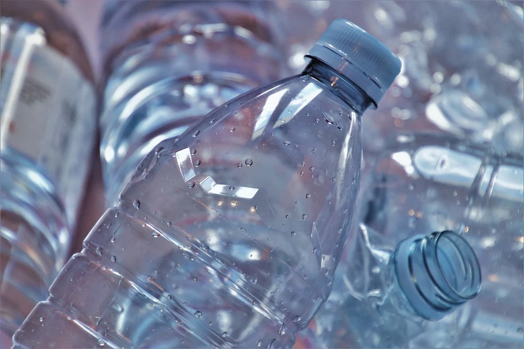 Fot. pixabay.com/ pasja1000 Plastikowe butelki wody mineralnej w zbliżeniu, ułożone w nieładzie z widocznymi kroplami wody na powierzchni.