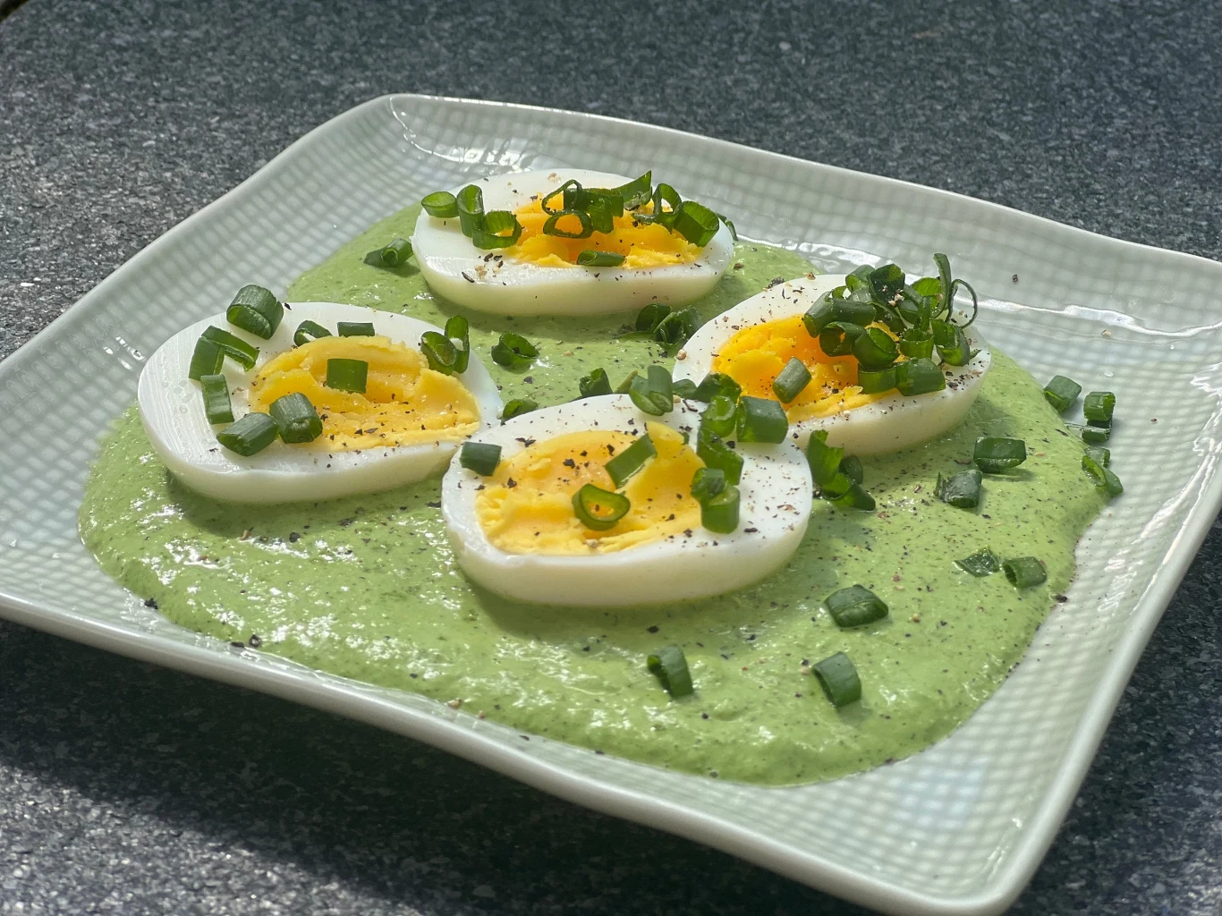 Jajka na sosie szczawiowym Talarki jajek na twardo ułożone na zielonym sosie ze świeżymi ziołami i kawałkami szczypiorku na przystawkowym talerzu.