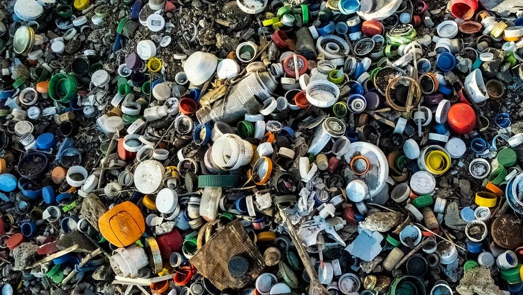 Fot. pixabay.com/ joshuatutu Stos kolorowych plastikowych nakrętek oraz innych odpadów plastikowych rozrzuconych na ziemi, przedstawiający problem zanieczyszczenia środowiska przez tworzywa sztuczne.