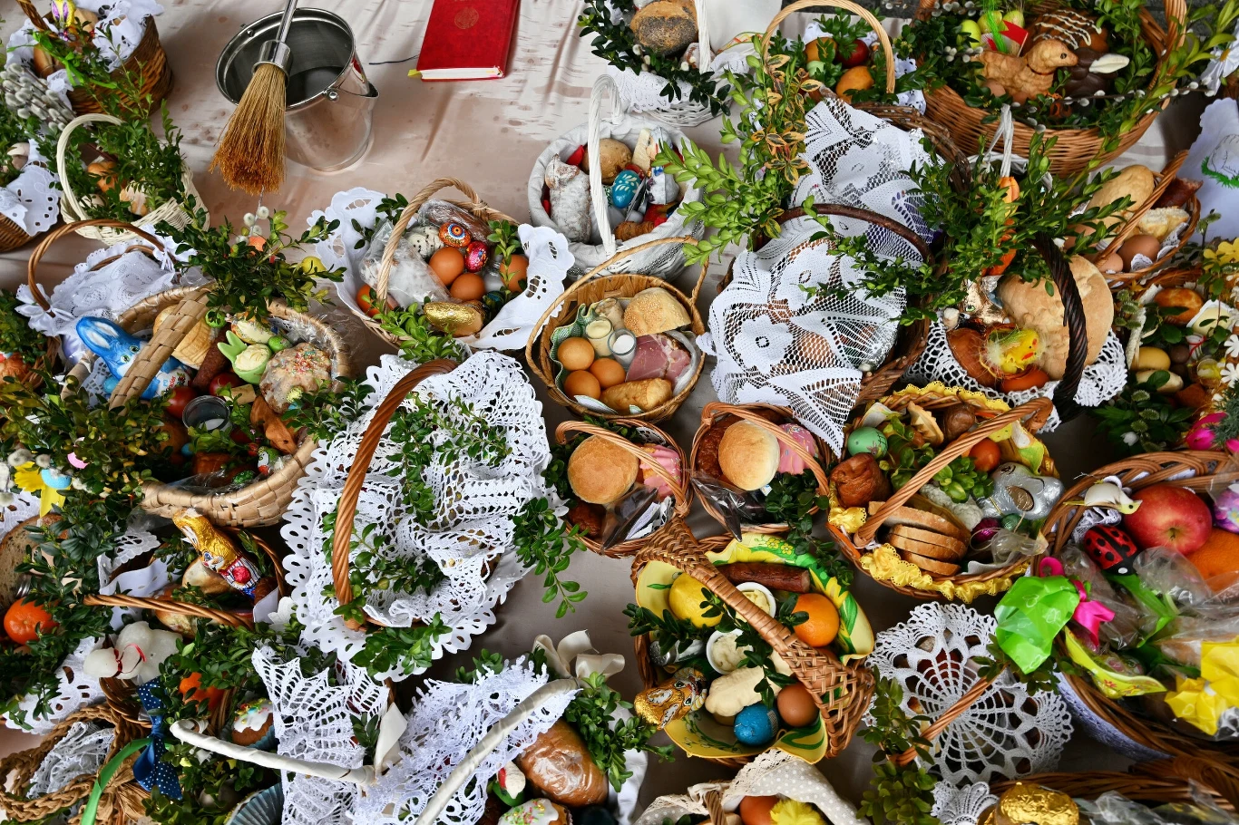 Tradycyjna święconka w Zakopanem Koszyki wielkanocne wypełnione pisankami, chlebem, kiełbasą i ciastkami, udekorowane zielonymi gałązkami i serwetkami z koronki, ustawione jedna obok drugiej na stole.