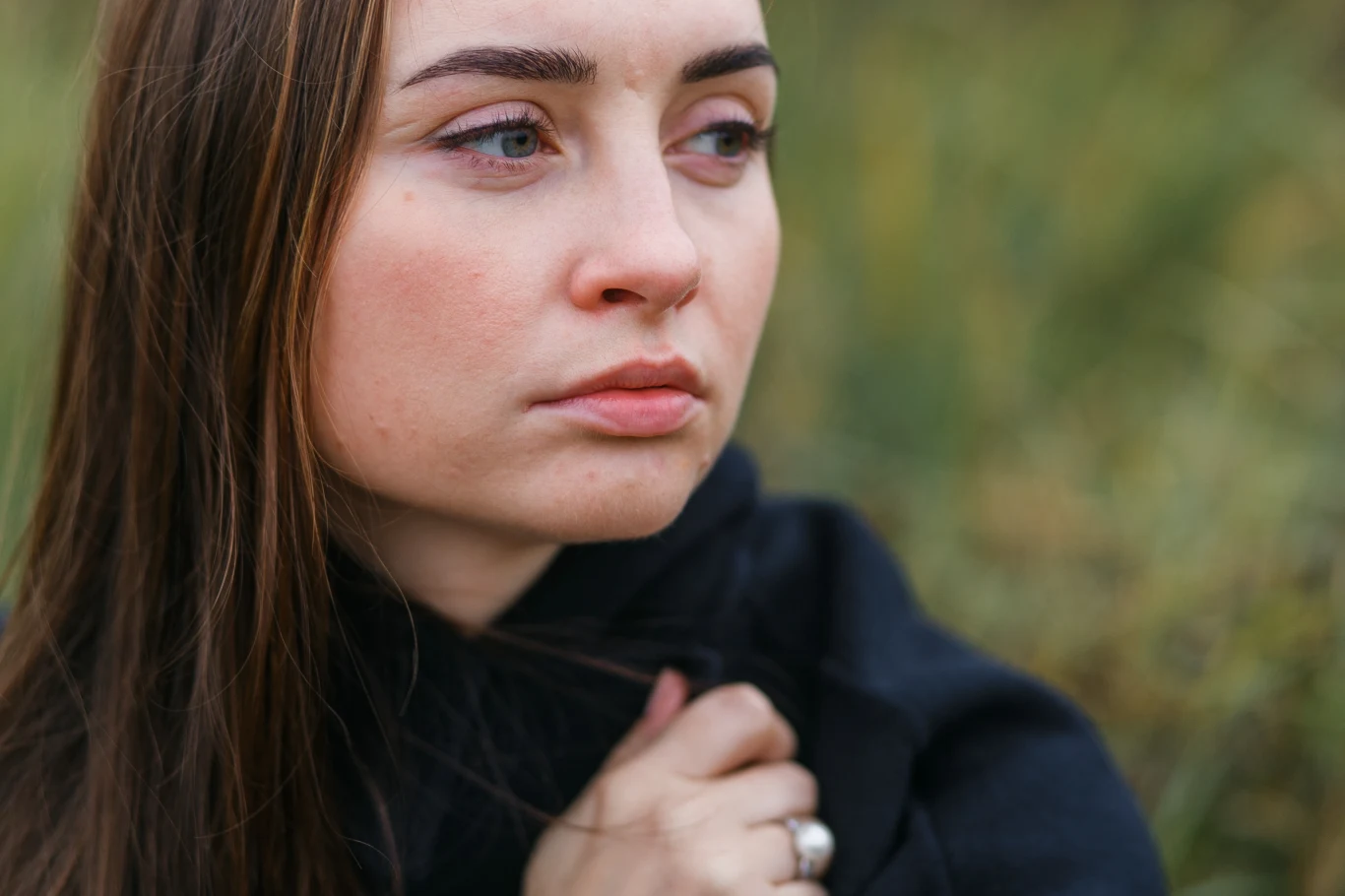 Strach przed zaangażowaniem można pokonać Zamyślona młoda kobieta patrzy w bok na tle przyrody, z nieco melancholijnym wyrazem twarzy. Ma długie włosy i ubrana jest w ciemny strój.