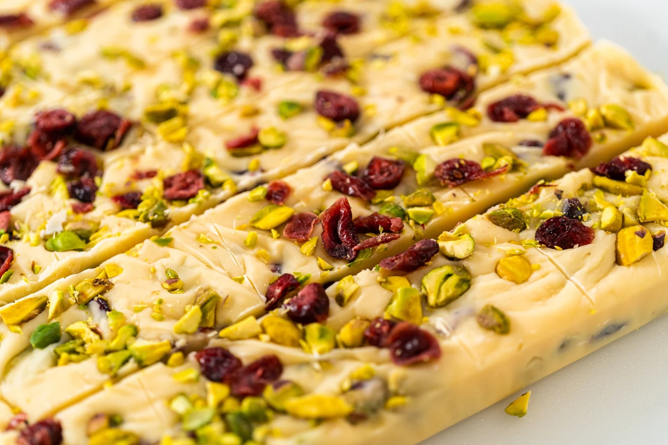 Przysmaki z dodatkiem pistacji to hit ostatnich lat Kawałki białej czekolady z dodatkiem pistacji i suszonej żurawiny, ułożone na jasnym tle.