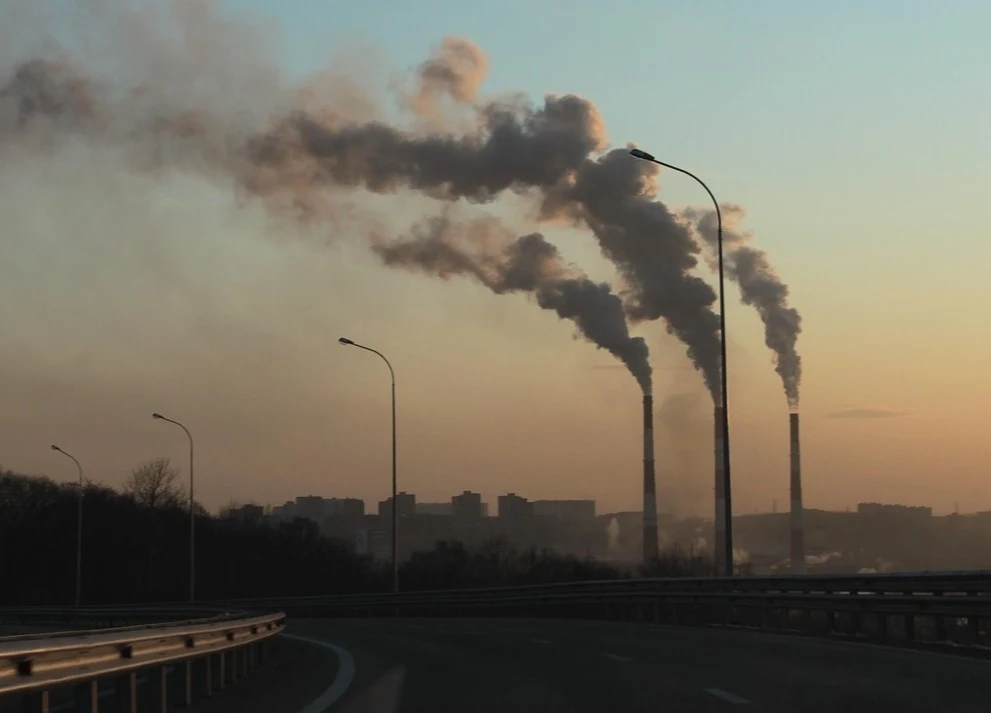 Fot. pixabay.com/ digifly840 Kominy przemysłowe emitujące gęste kłęby dymu unoszące się na tle miasta o zmierzchu.