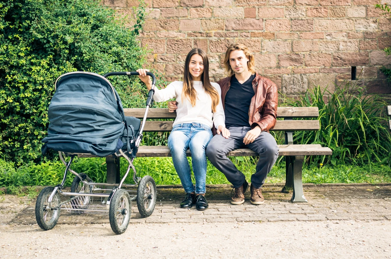 Kryzys demograficzny w Europie Środkowo - Wschodniej. W Polsce liczba osób w wieku produkcyjnym ma spaść o prawie 6 proc. Młoda para siedzi na ławce w parku, obok nich wózek dziecięcy. Zarówno mężczyzna, jak i kobieta są uśmiechnięci i wyglądają na zrelaksowanych. Otoczenie jest zielone i spokojne, co sugeruje miłą atmosferę wypoczynku.