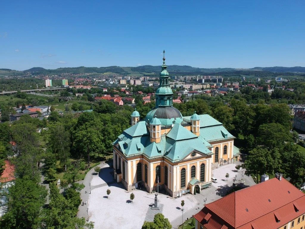 Kościół z zieloną kopułą otoczony ogrodem, z widokiem na miasto i góry w tle.