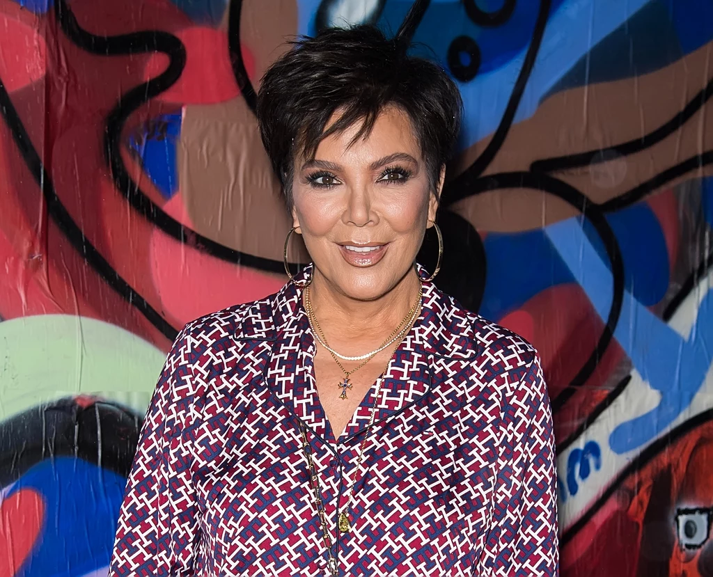 Opinie na temat zdjęć Kris Jenner na jej Instagramie są podzielone. Jedni są zachwyceni, inni uważają, że zdecydowanie przesadza z przeróbkami Osoba stojąca przed kolorowym tłem graffiti, ubrana w wzorzystą koszulę i uśmiechająca się do aparatu.