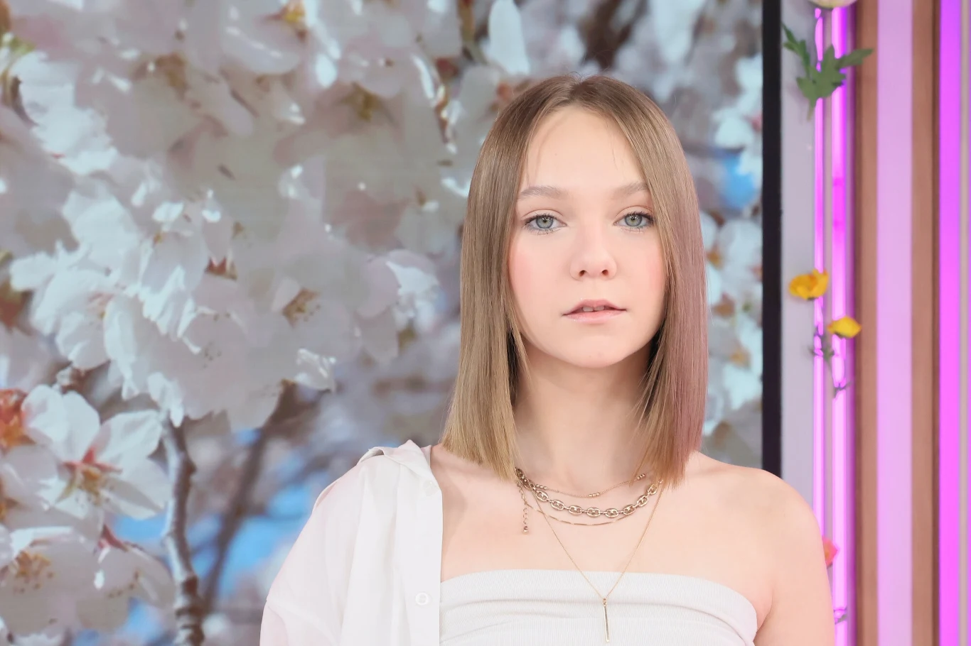 Maja Krzyżewska prezentuje nowy teledysk Młoda kobieta z prostymi, blond włosami, ubrana w białą bluzkę na jednym ramieniu, stoi na tle kwitnących kwiatów wiśni. W tle widoczne są różowe i fioletowe barwy oraz zielone i pomarańczowe dekoracje kojarzące się z wiosną.
