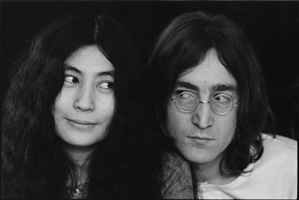Yoko Ono i John Lennon Dwie postaci patrzą na siebie z bliska, widzimy ich twarze, jedna z osób nosi okulary. Zdjęcie w czerni i bieli tworzy intymną atmosferę.
