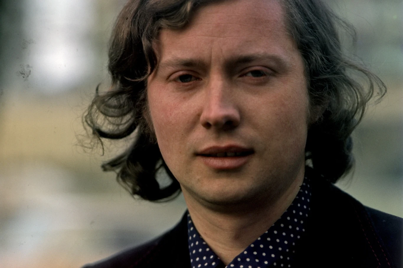 Marek Grechuta nagrał przebój "Wiosna, ach to ty" Portret mężczyzny w średnim wieku z kręconymi włosami, ubrany w ciemną marynarkę i koszulę w kropki, na jednolitym tle.