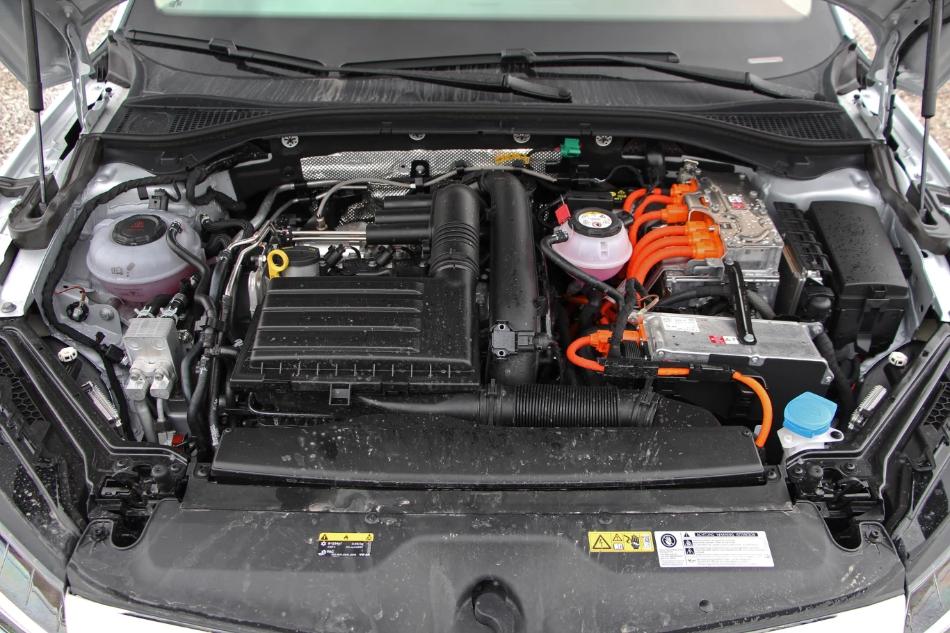 Jaki silnik jest najlepszy w Skodzie Superb III? Silnik hybrydowy samochodowy z wyraźnymi elementami mechaniki i elektryki, takimi jak okablowanie i komponenty elektroniczne, widoczny w otwartej komorze silnikowej.