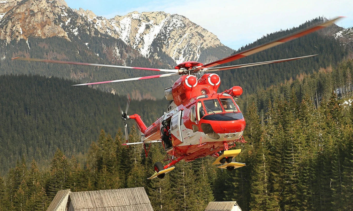 Tatry. Dwa groźne wypadki. Interweniowało LPR Czerwony helikopter ratunkowy unoszący się nad górskim krajobrazem z widokiem na las i ośnieżone szczyty w tle.