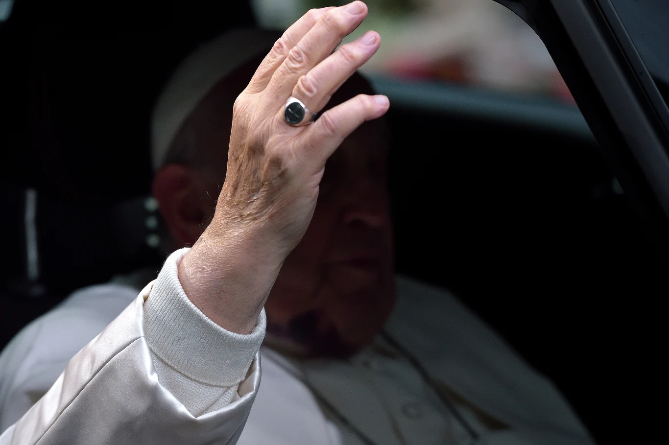 Pierścień Rybaka papieża Franciszka. Jego zniszczenie kończy pontyfikat i zaczyna sede vacante Ręka w eleganckiej białej sutannie z pierścieniem uniesiona ponad głową w geście błogosławieństwa. Postać jest częściowo ukryta w cieniu samochodu.